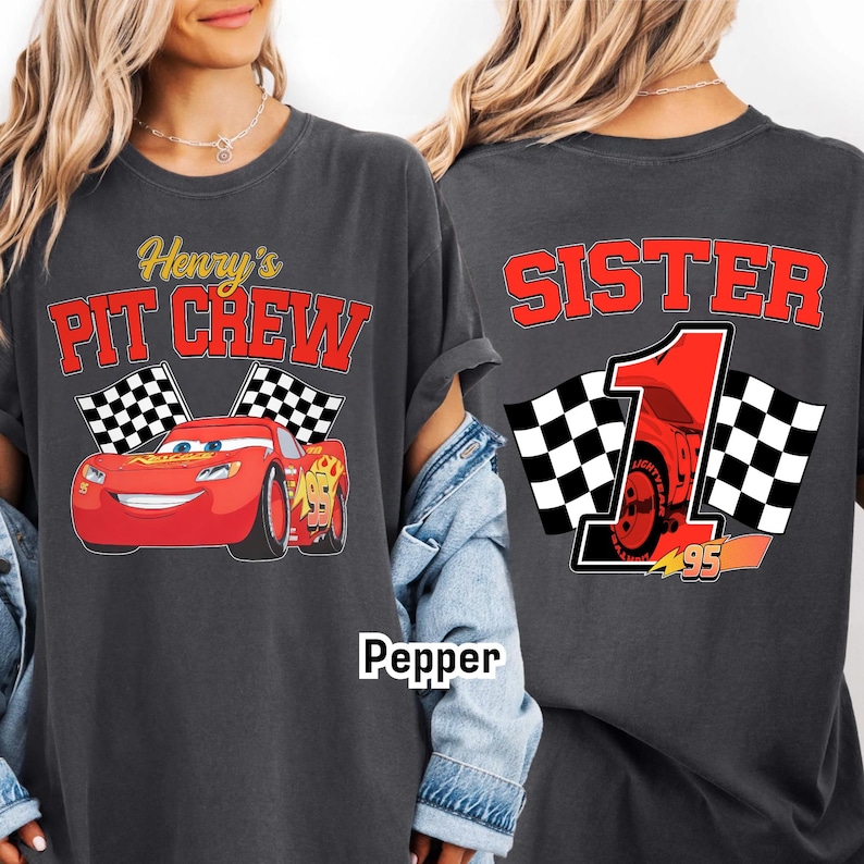 May include: Dark gray t-shirt featuring a red race car graphic with the text "Henry's Pit Crew" on the front. The back of the shirt says "Sister 1" with a race car graphic and checkered flags.