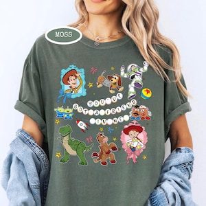 May include: Moss green t-shirt featuring a colorful graphic of characters from the movie Toy Story. The phrase "You've Got a Friend in Me" is displayed in the center. The shirt has short sleeves and a relaxed fit.