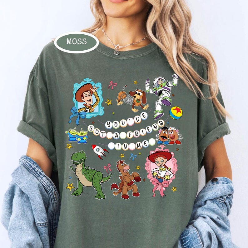 May include: Moss green t-shirt featuring a colorful graphic of characters from the movie Toy Story. The phrase "You've Got a Friend in Me" is displayed in the center. The shirt has short sleeves and a relaxed fit.