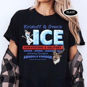 Op de afbeelding: Zwart T-shirt met de blauwe tekst "Kristoff & Sven's ICE", met Olaf de sneeuwpop en Sven de rendier graphics. Het shirt bevat ook de tekst "Harvesting & Delivery" en "Arendelle Kingdom". Het woord "BLACK" staat in een witte ovaal.