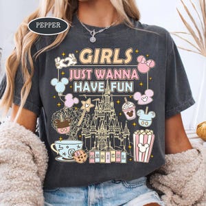 May include: Dark gray t-shirt with the text "GIRLS JUST WANNA HAVE FUN" and a graphic of a castle, Mickey Mouse balloons, and other Disney-themed images. The word "MAGICAL" is at the bottom. The shirt is a crew neck.