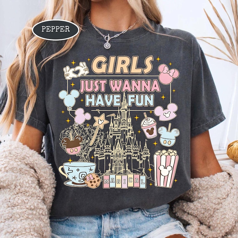 May include: Dark gray t-shirt with the text "GIRLS JUST WANNA HAVE FUN" and a graphic of a castle, Mickey Mouse balloons, and other Disney-themed images. The word "MAGICAL" is at the bottom. The shirt is a crew neck.