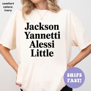 May include: Ivory-colored t-shirt with the names "Jackson, Yannetti, Alessi, Little" printed in bold black letters. The shirt also has the text "comfort colors: ivory" and a purple circle with the words "SHIPS FAST!"