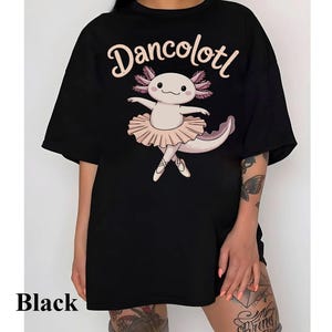 May include: Black oversized t-shirt with a graphic of a pink axolotl wearing a pink tutu and ballet shoes. The text "Dancolottl" is printed on the shirt.