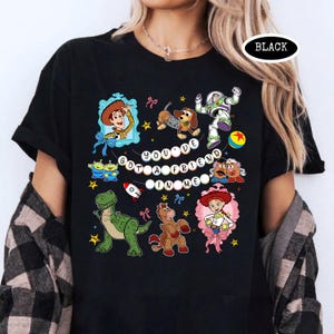 May include: Black t-shirt featuring colorful cartoon characters and the text "You've Got a Friend in Me." The design includes Woody, Buzz Lightyear, and other characters from the animated movie.