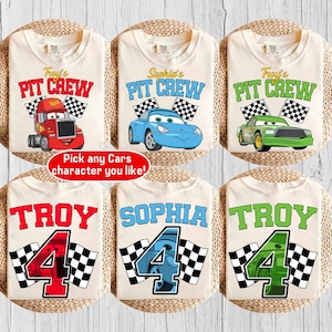 May include: Six cream-colored t-shirts with racing-themed designs. The shirts feature the text "Troy's PIT CREW", "Sophia's PIT CREW", and "Troy's PIT CREW" with car graphics. Other shirts have the names "TROY" and "SOPHIA" with the number "4" and checkered flags.