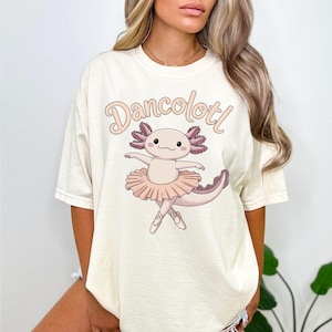 May include: A white t-shirt with a pink axolotl wearing a pink tutu and the text "Dancolottl" printed on the front.
