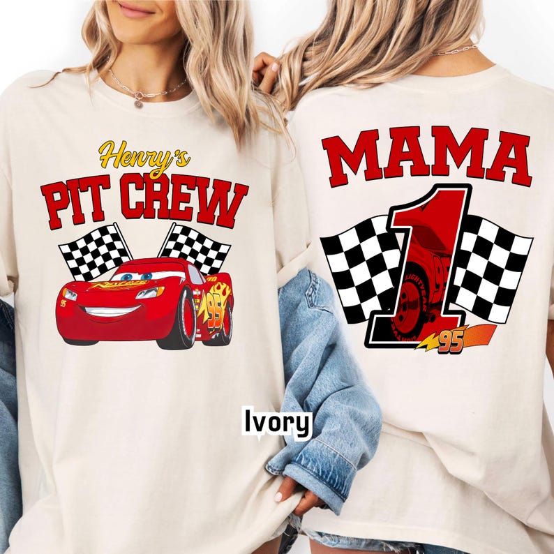 May include: Ivory-colored t-shirts with racing-themed graphics. One shirt features "Henry's Pit Crew" with a red race car and checkered flags. The other shirt displays "MAMA 1" with a race car and checkered flags. The number "95" is also visible.