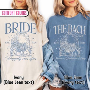 May include: Two long-sleeved t-shirts, one ivory and one blue jean, with matching graphics. The ivory shirt says "BRIDE" above a globe design and "Happily ever after." The blue jean shirt says "THE BACH Club" and "Victoria's Bachelorette Party."