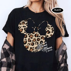 May include: Black t-shirt with a Minnie Mouse design in a leopard print pattern. The design includes the text "Minnie Mouse xoxo" in a cursive font. The word "BLACK" is printed in a white oval.