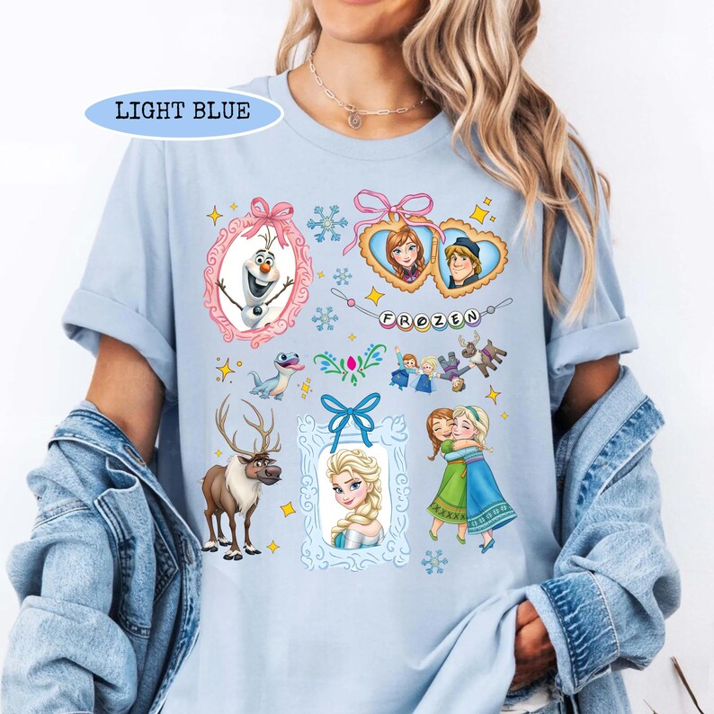 Puede incluir: Camiseta azul claro con varios personajes y elementos de la pel&iacute;cula animada "Frozen". El dise&ntilde;o incluye im&aacute;genes de Olaf, Anna, Elsa, Kristoff y Sven, junto con la palabra "FROZEN" y marcos decorativos y copos de nieve.