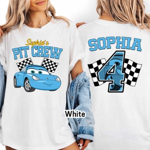 May include: White t-shirt featuring a blue cartoon car with the text "Sophia's PIT CREW" and checkered flags. The back of the shirt displays the name "SOPHIA" and the number "4" with a car design and checkered flags.
