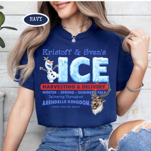 Op de afbeelding: Marineblauw T-shirt met de tekst "Kristoff & Sven's ICE" en illustraties van Olaf en Sven. Het shirt bevat ook tekst over oogsten en levering uit het koninkrijk Arendelle.