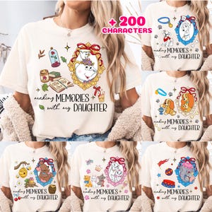 May include: A cream-colored t-shirt featuring various Disney-themed graphic prints, including characters like Mrs. Potts, Chip, and other animated figures in ornate frames, with the text "making MEMORIES with my DAUGHTER" printed in black script.