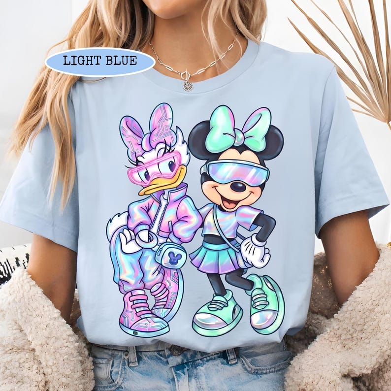 May include: Light blue t-shirt featuring Daisy Duck and Minnie Mouse in futuristic outfits. The shirt has the text "LIGHT BLUE" in a light blue oval. The cartoon characters are wearing sunglasses and sneakers.