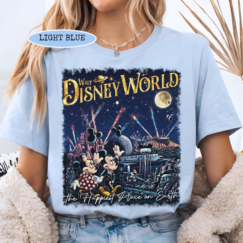 May include: Light blue t-shirt featuring a colorful graphic of Walt Disney World at night, with fireworks, Mickey and Minnie Mouse, and the text "Walt Disney World" and "the Happiest Place on Earth."