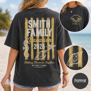 May include: A charcoal gray t-shirt featuring a back graphic with vertical gold stripes, a seahorse, a starfish, and a seashell. Text reads: SMITH FAMILY Vacation 2026, Making Memories Together, KEY WEST, FLORIDA. Front chest has a small sunset graphic.