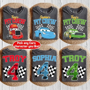 May include: Six gray t-shirts with racing-themed designs. Three shirts feature the text "Pit Crew" with different car graphics and names. The other three shirts display names and the number "4" with checkered flags. The text "Pick any Cars character you like!" is also present.