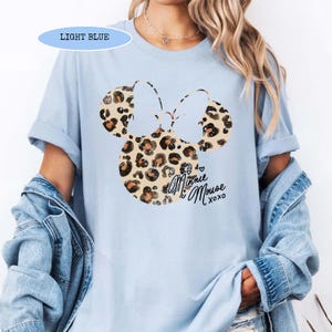 May include: Light blue t-shirt with a Minnie Mouse design. The design features a leopard print bow and the words "Minnie Mouse xoxo". The shirt is a light blue colour.