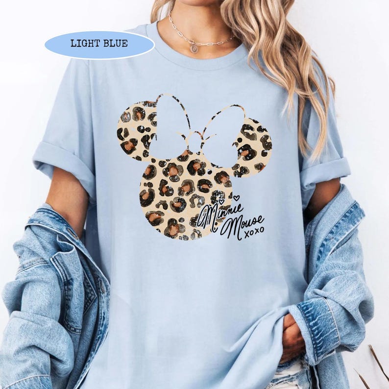 May include: Light blue t-shirt with a Minnie Mouse design. The design features a leopard print bow and the words "Minnie Mouse xoxo". The shirt is a light blue colour.