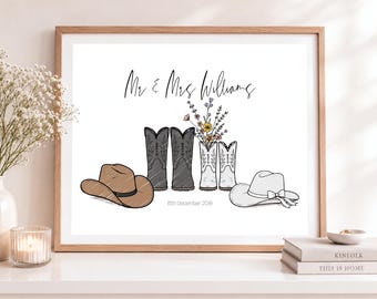 May include: A framed print featuring the text Mr & Mrs Williams and 15th December 2018. The illustration includes a brown cowboy hat, a pair of black cowboy boots, a pair of white cowboy boots holding colorful wildflowers, and a white cowboy hat.