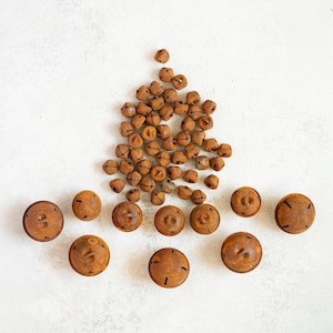 Op de afbeelding: Een verzameling kleine, roestbruine metalen belletjes en grotere, vergelijkbaar gekleurde ronde objecten met een kruisvormig ontwerp. De belletjes zijn geclusterd, terwijl de ronde objecten in een rij zijn gerangschikt. Op een witte ondergrond.