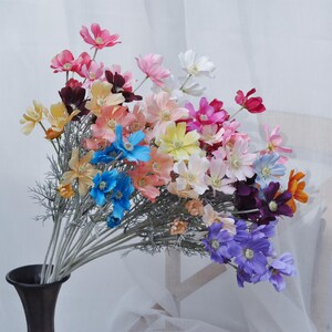 Könnte beinhalten: Ein Strauß künstlicher Blumen in verschiedenen Farben, darunter Rosa, Blau, Lila, Gelb und Weiß. Die Blumen sind in einer Vase arrangiert und haben ein realistisches Aussehen.