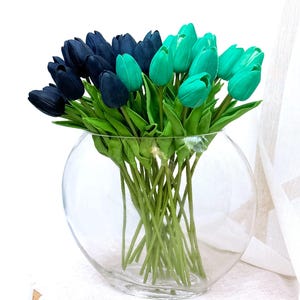 Puede incluir: Un jarrón de vidrio lleno de un ramo de tulipanes artificiales. Los tulipanes son una mezcla de azul oscuro y turquesa.