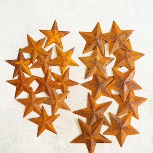 May include: A collection of rustic, metal stars in varying sizes, arranged on a light-colored surface. The stars have a weathered, orange-brown finish, suggesting an aged or antique appearance. Ideal for home decor or craft projects.