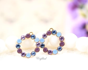 Puede incluir: Dos pendientes de aro dorados, cada uno adornado con un círculo de gemas de colores. Las gemas son en tonos morado, azul y celeste. Los pendientes están sobre un fondo borroso con el texto "Waytobead".