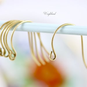 May include: A set of gold-toned metal earring hooks with a curved design and a small loop at the bottom for attaching jewellery components. The hooks are suspended on a light blue rod, and the text Waytobead is visible in the upper centre.