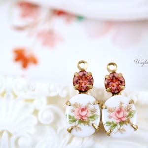 May include: A pair of gold-tone earrings with a white porcelain charm featuring a pink floral design and a pink crystal accent.