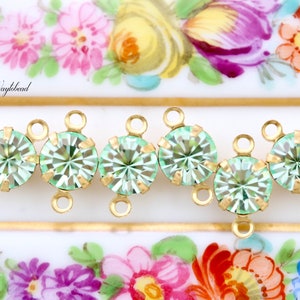 Puede incluir: Cinco cuentas de cristal verde claro con engastes y lazos de metal dorado. Las cuentas están dispuestas en fila y están conectadas por los lazos.