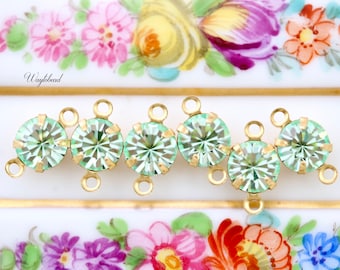Puede incluir: Cinco cuentas de cristal verde claro con engastes y lazos de metal dorado. Las cuentas están dispuestas en fila y están conectadas por los lazos.