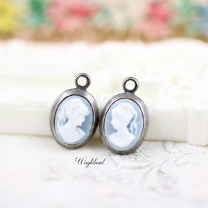 May include: Two silver oval-shaped charms with a blue cameo of a woman's profile. The charms have a loop at the top for attaching to a necklace or bracelet.