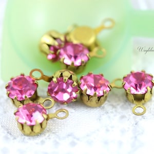 May include: A group of pink rhinestone embellishments with gold metal settings and loops. The rhinestones are faceted and have a shiny finish.