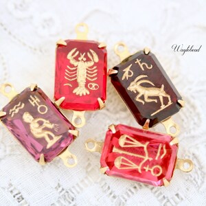 May include: Four gold-tone zodiac charm pendants with red and purple glass insets. The charms feature the astrological signs of Scorpio, Capricorn, Aquarius, and Libra.