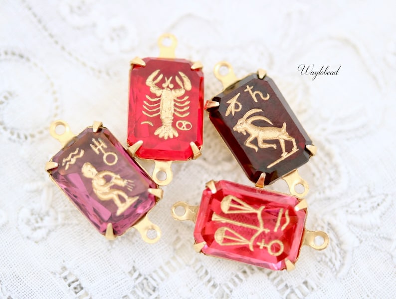 May include: Four gold-tone zodiac charm pendants with red and purple glass insets. The charms feature the astrological signs of Scorpio, Capricorn, Aquarius, and Libra.
