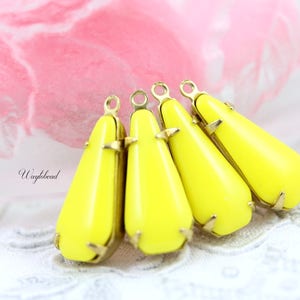 May include: Four yellow teardrop-shaped glass beads with gold-tone metal caps and loops. The beads are arranged in a row, with the caps facing the viewer.