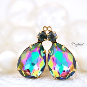 May include: Two iridescent teardrop-shaped crystal pendants with gold-tone metal settings and black accents. The pendants are hanging from a white background.