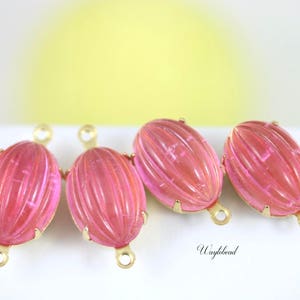 May include: Four pink glass oval beads with gold metal caps and loops. The beads have a ribbed texture.