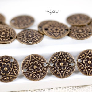 May include: A group of 10 antique gold metal round charms with a floral design and two holes. The charms are on a white surface.