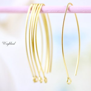 Może przedstawiać: Pięć złotych obręczy z drutu z pętlą na końcu. Obręcze wiszą na różowej powierzchni.