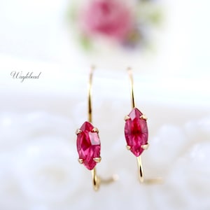 May include: A pair of gold hoop earrings with a marquise-shaped red gemstone in each hoop.
