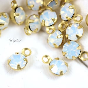 May include: A close-up of a group of gold-toned metal charms with clear, iridescent opal-like stones. The charms have a loop at the top for attaching to jewelry or other crafts.