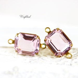 以下が含まれることがあります： 金色の金属製のセッティングとジャンプリングが付いた、薄いピンク色のガラスのエメラルド型の接続チャームが2つです。