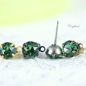 May include: Two pairs of green crystal earrings with gold and silver settings. The earrings are shown on a white lace background. The text "Waybead" is visible in the image.