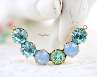 Puede incluir: Un componente de joyería curvado con piedras de cristal azul claro y azul pálido engastadas en metal dorado. Los cristales varían en tamaño y forma, con una piedra turquesa central. El texto "Waytobead" es visible.