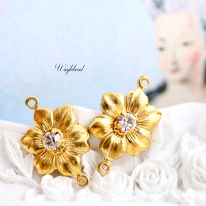 May include: Two gold-tone flower-shaped charms with clear rhinestone centers. Each charm has two jump rings for attaching to jewelry.