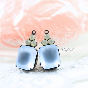 May include: A pair of light blue square glass earrings with a black metal frame and a cluster of clear rhinestones at the top. The earrings are on a white surface.